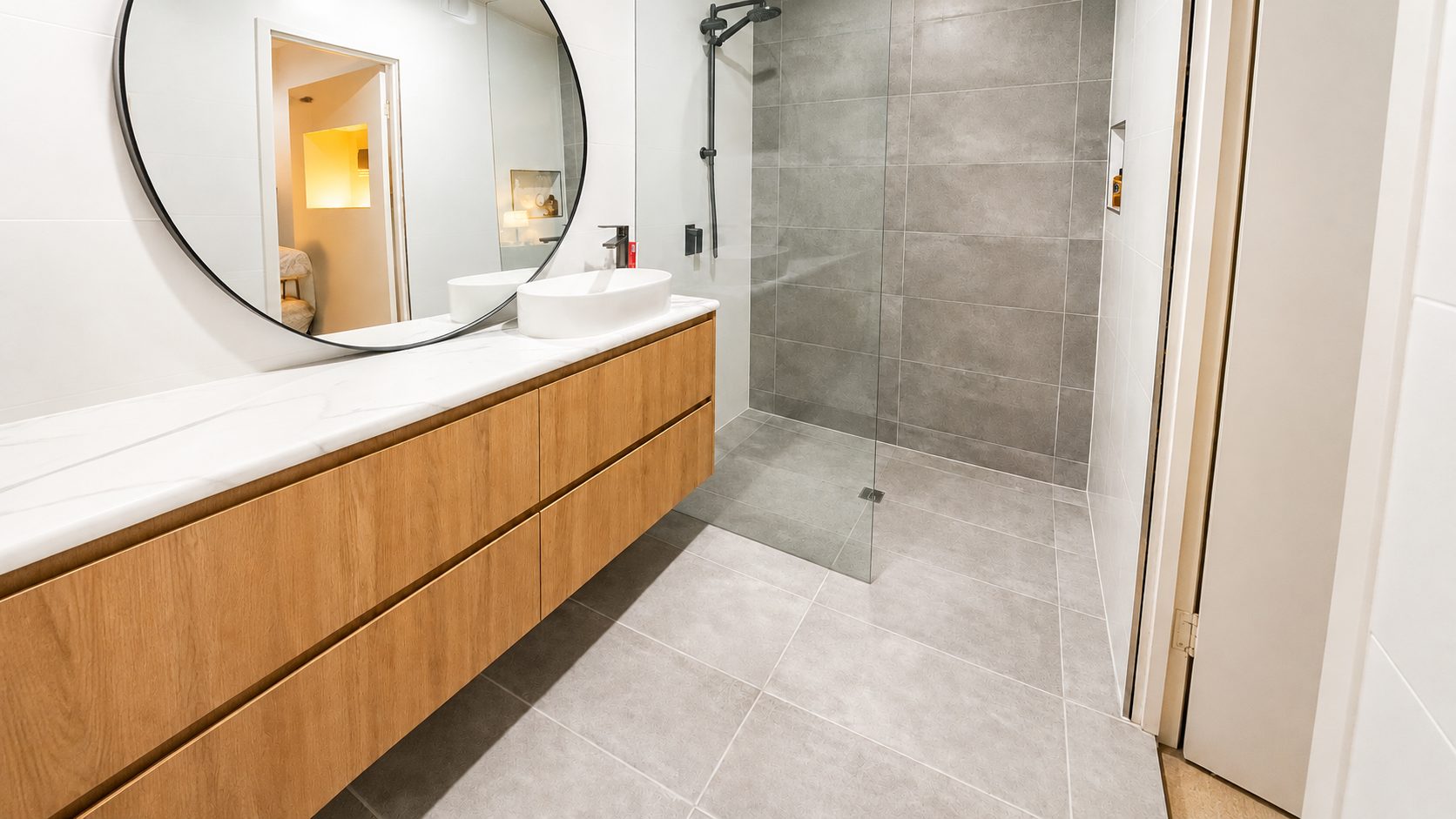 Floating timber vanity with a stone top, round black mirror and walk-in shower