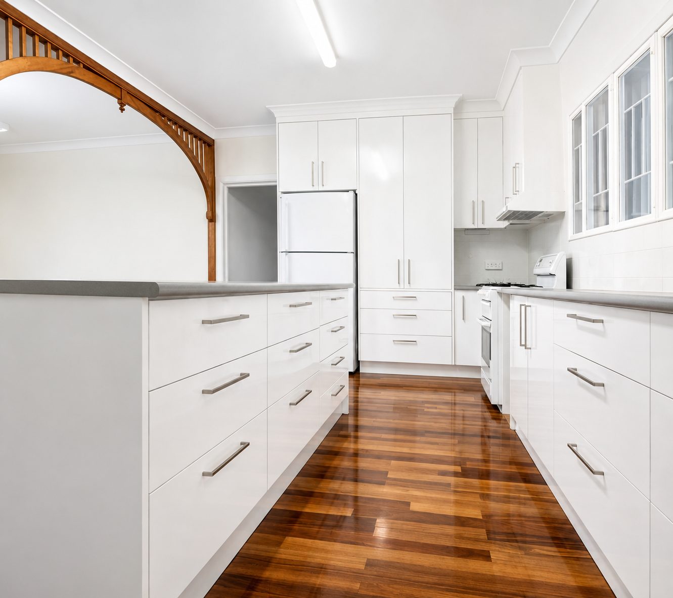 The finished kitchen: bright white cabinetry, stone benchtops and polished timber floors