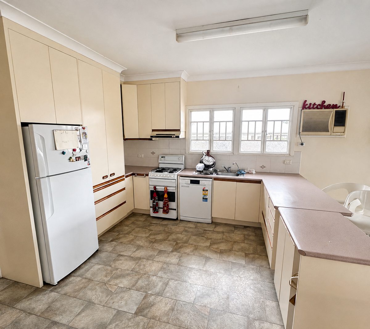 The same kitchen before work: dated cream cabinetry, laminate benchtops and vinyl floor